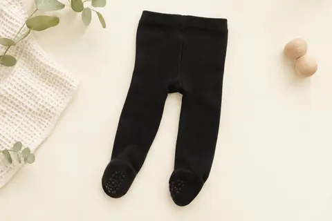 Collant bébé noir uni posé à plat, avec maille extensible et zones antidérapantes sous les pieds