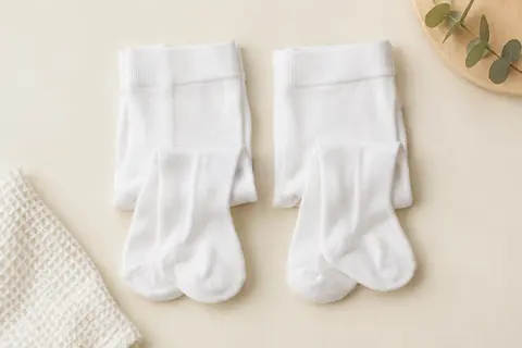 Deux paires de collants bébé blancs et opaques, pliées sur un fond crème avec du coton gaufré.