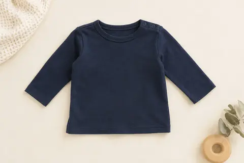 Tee-shirt bébé bleu foncé à manches longues, posé à plat sur un fond crème avec du coton gaufré.